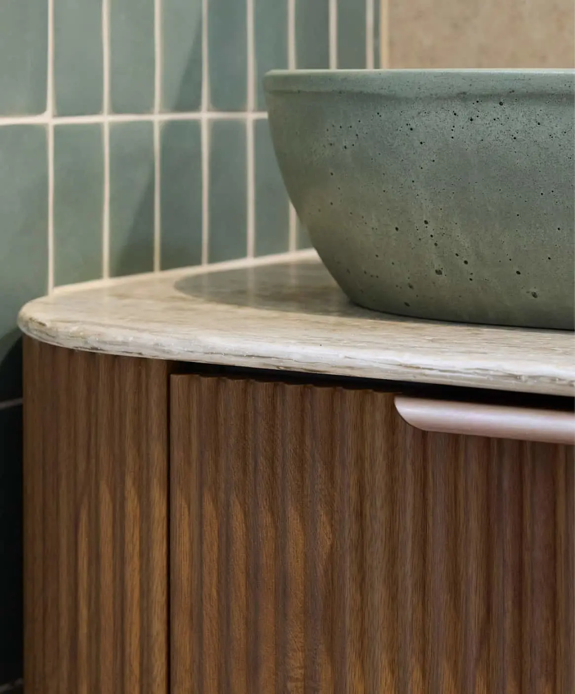 Sage green concrete basin on wooden vanity with light marble top, against teal vertical tile backsplash.