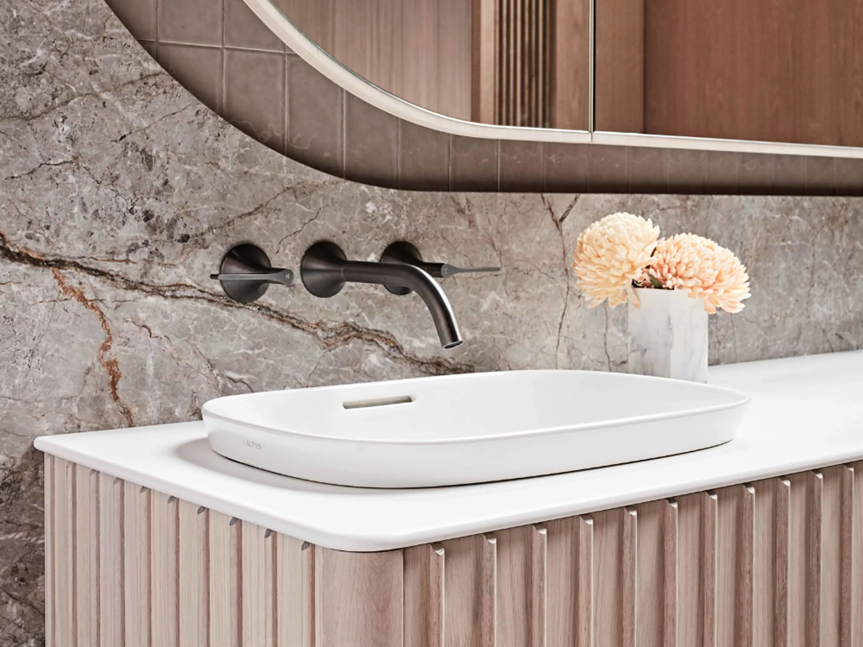 Modern bathroom with white vessel sink, wall-mounted black faucet, marble backsplash, and peach flowers in a small vase.