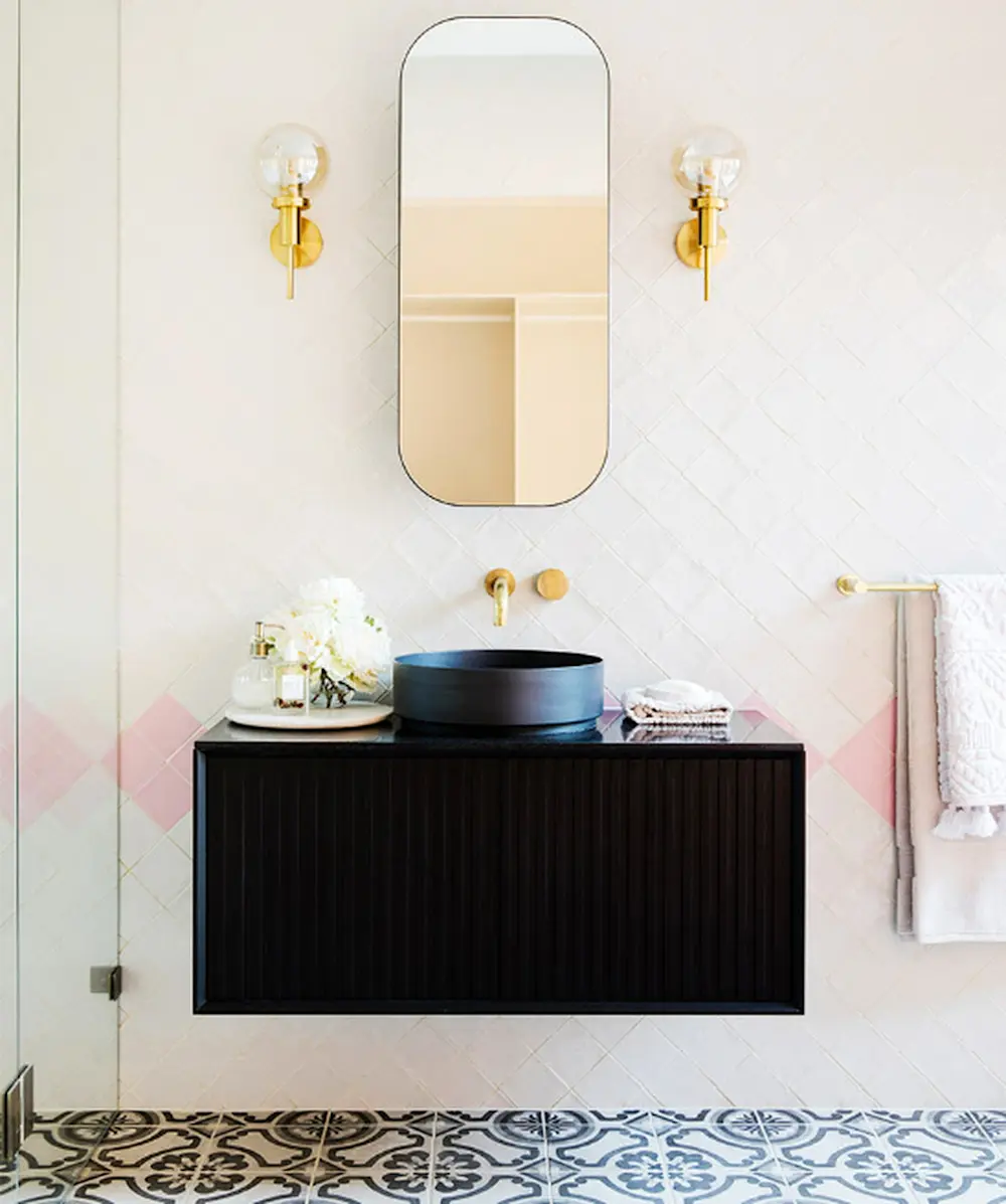 Modern bathroom with black floating vanity, round vessel sink, oval mirror, brass sconces, and patterned floor tiles.