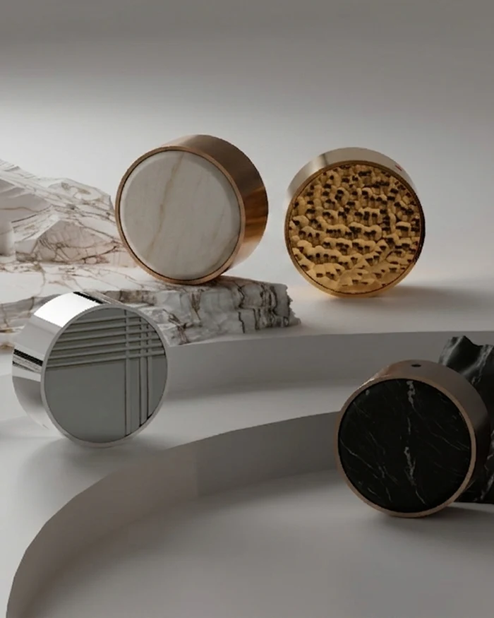 Three circular basin mixers in silver, gold, and black marble finishes displayed on a white surface with marble slabs.