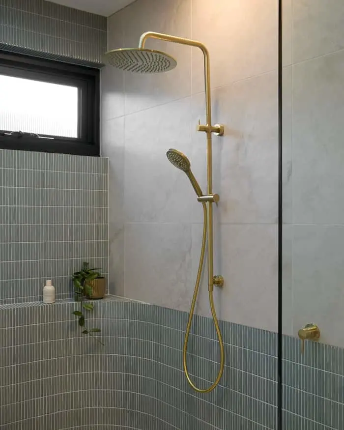 Modern bathroom shower with brass fixtures, round rainhead and handheld sprayer against marble and teal tiled walls.