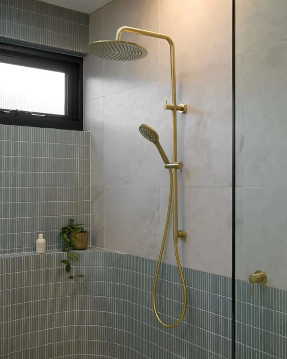 Modern bathroom shower with brass fixtures, round rainhead and handheld sprayer against marble and teal tiled walls.