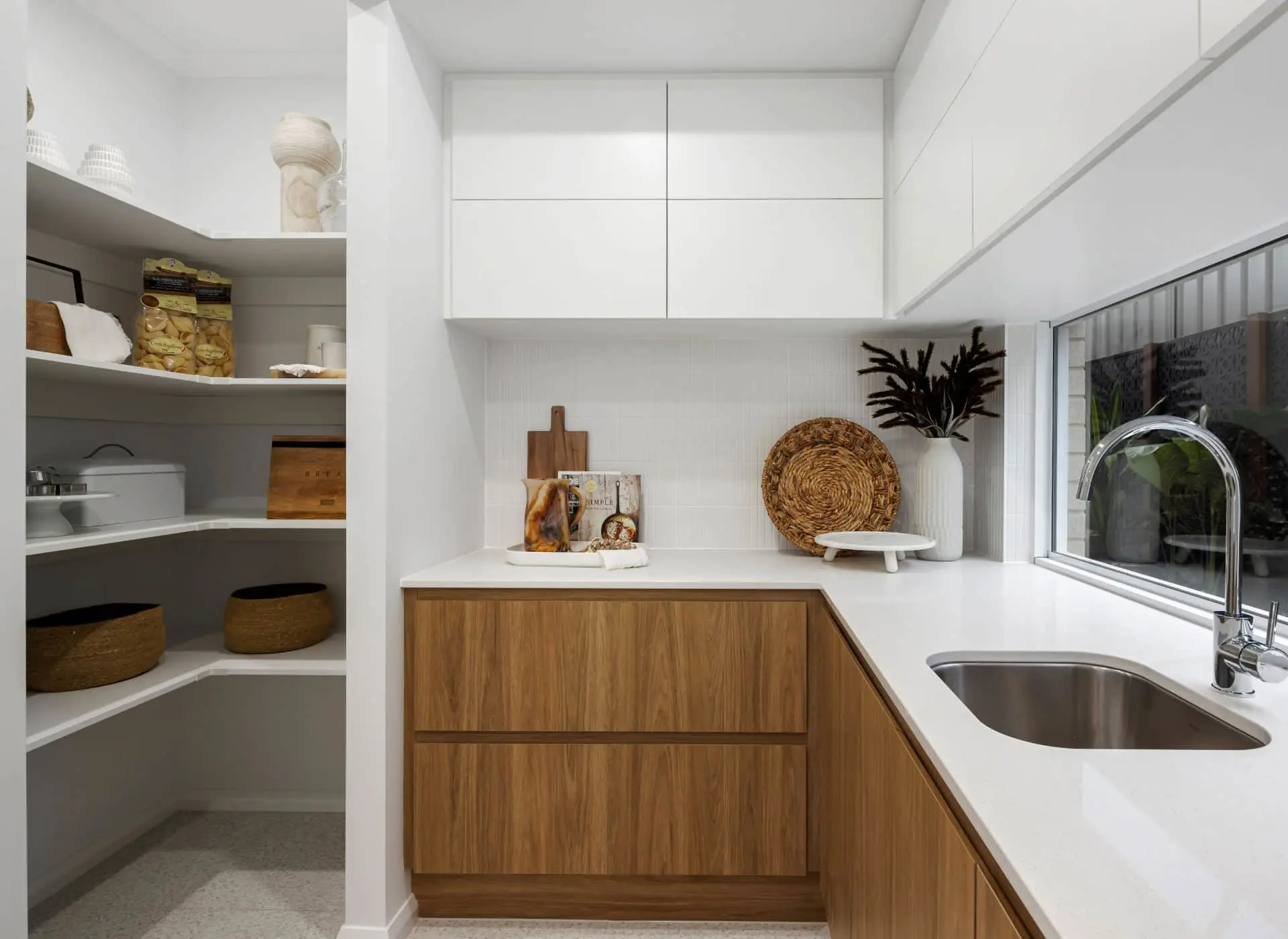 Modern kitchen with wood cabinets, white countertops, and adjacent pantry with shelving and woven baskets.