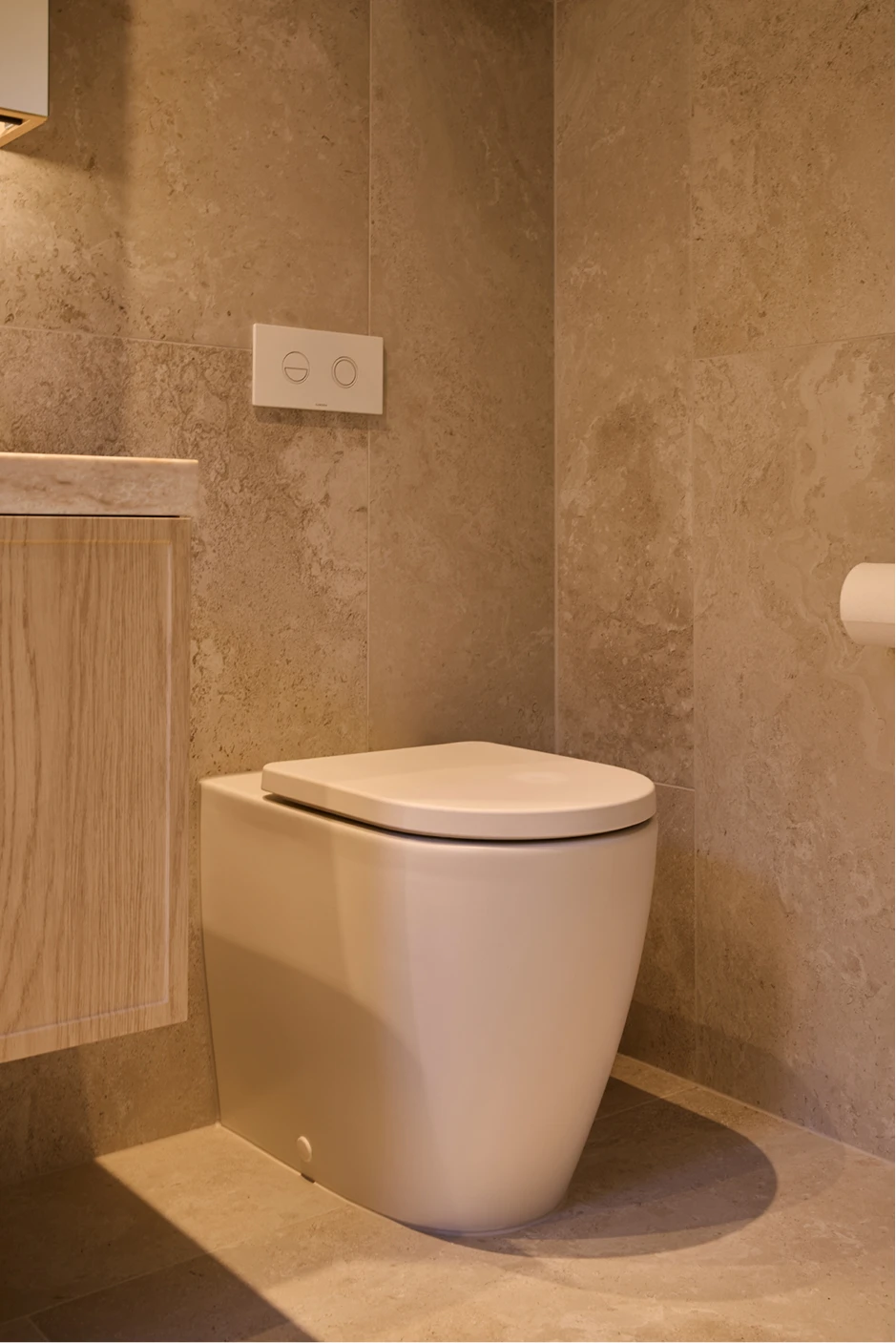 Modern bathroom with white toilet, beige textured walls, wooden vanity, and wall-mounted flush panel.
