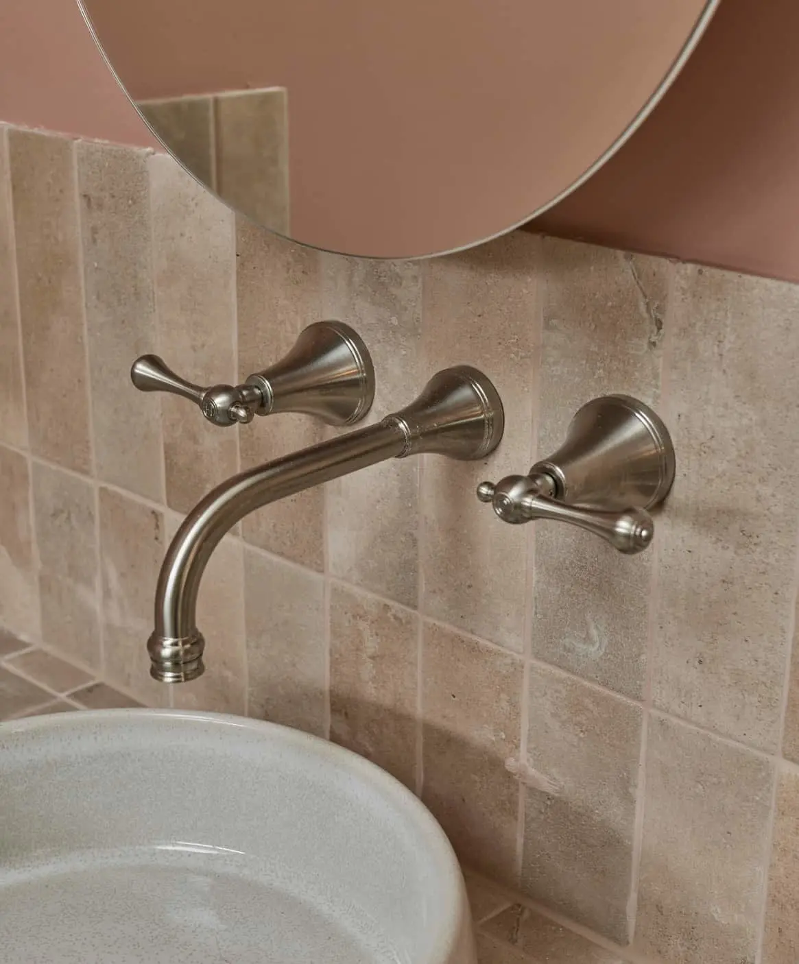 Wall-mounted bathroom faucet with ceramic sink on left, on pale pink tile backsplash.
