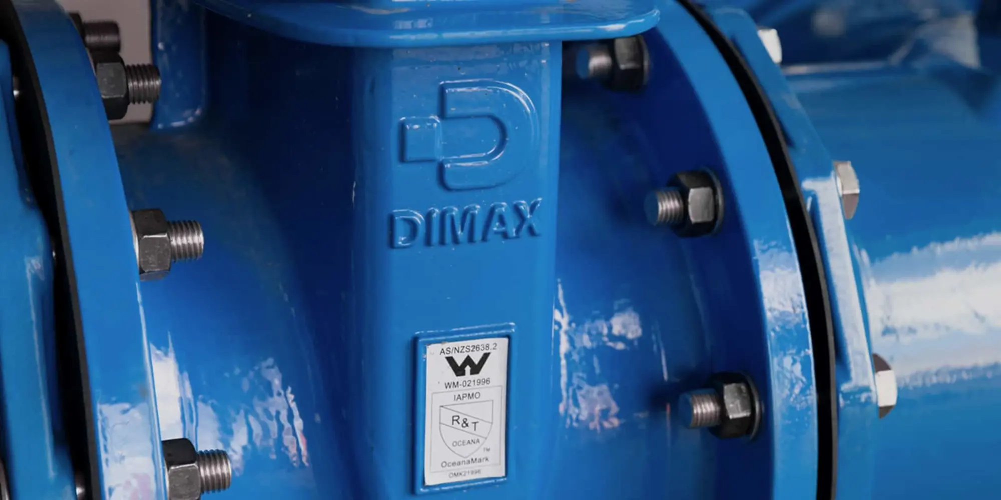 Close-up of blue DIMAX industrial pipe fitting with bolted flanges and certification label.