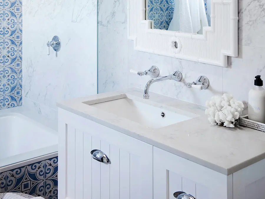 Elegant bathroom with white marble vanity, blue decorative tiles, wall-mounted faucet, and white coral decoration.