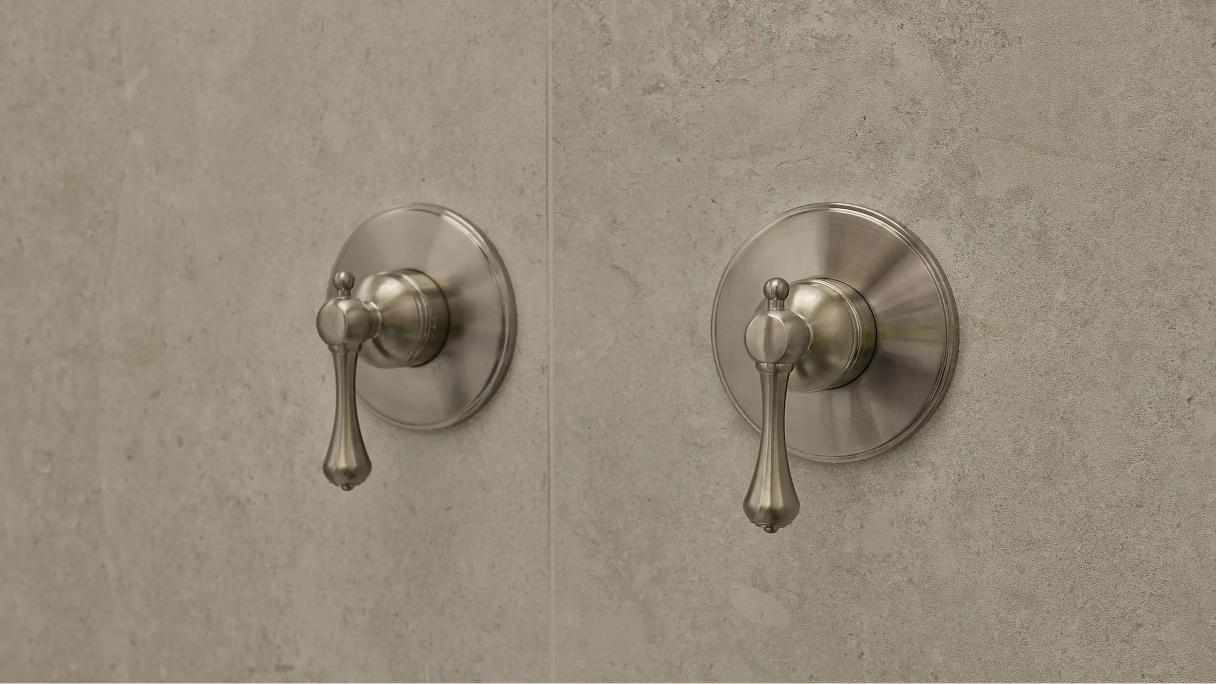 Two brushed nickel shower handles with teardrop-shaped levers mounted on a beige stone wall.