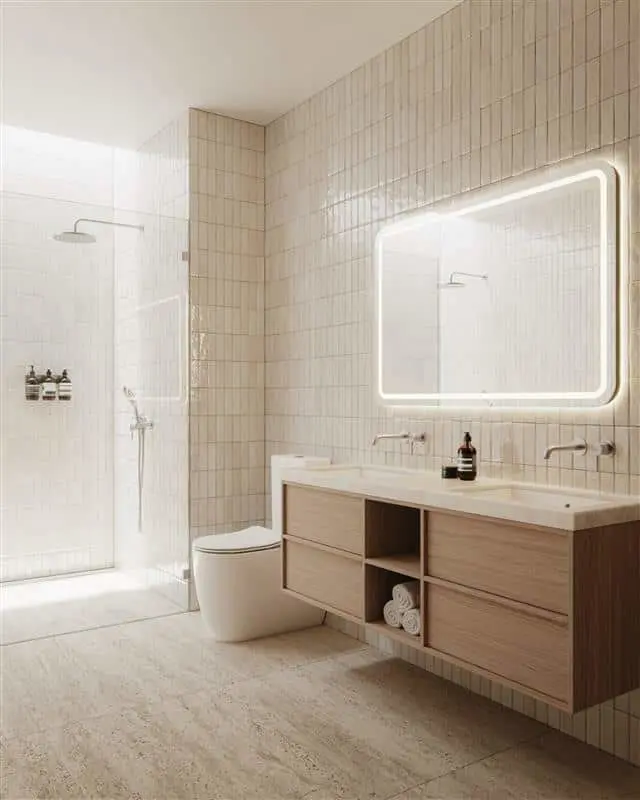 Modern bathroom with beige tile walls, glass shower, wooden floating vanity, illuminated mirror, and white toilet.