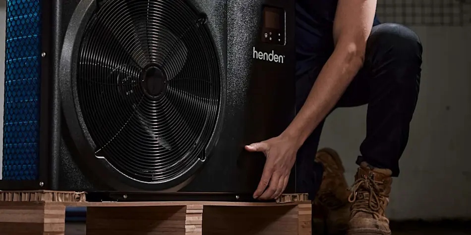Person installing a Henden heat pump unit on a wooden platform, with the fan component visible.