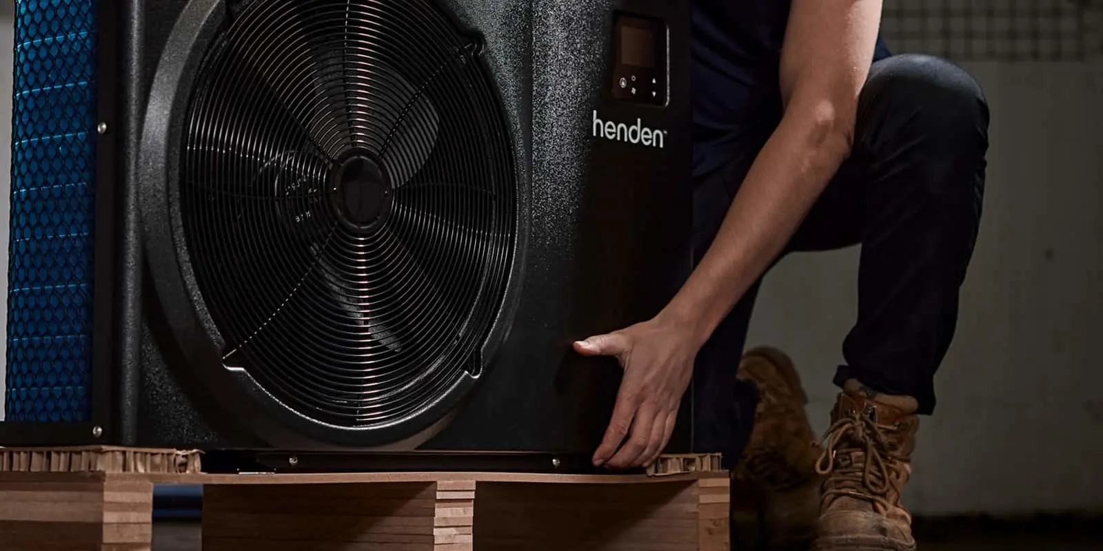 Person installing a Henden heat pump unit on a wooden platform, with the fan component visible.