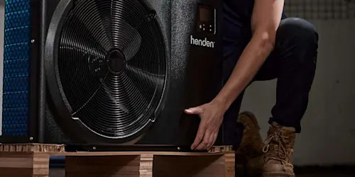 Person installing a Henden heat pump unit on a wooden platform, with the fan component visible.