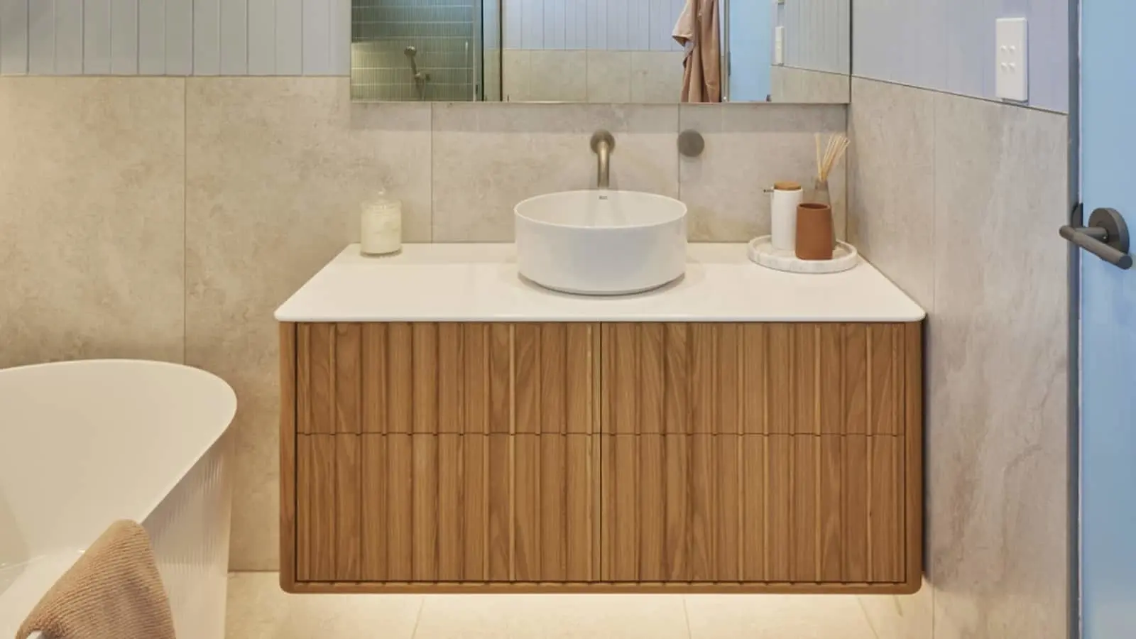 Modern bathroom with wooden vanity, white vessel sink, marble walls, and minimalist accessories on white countertop.