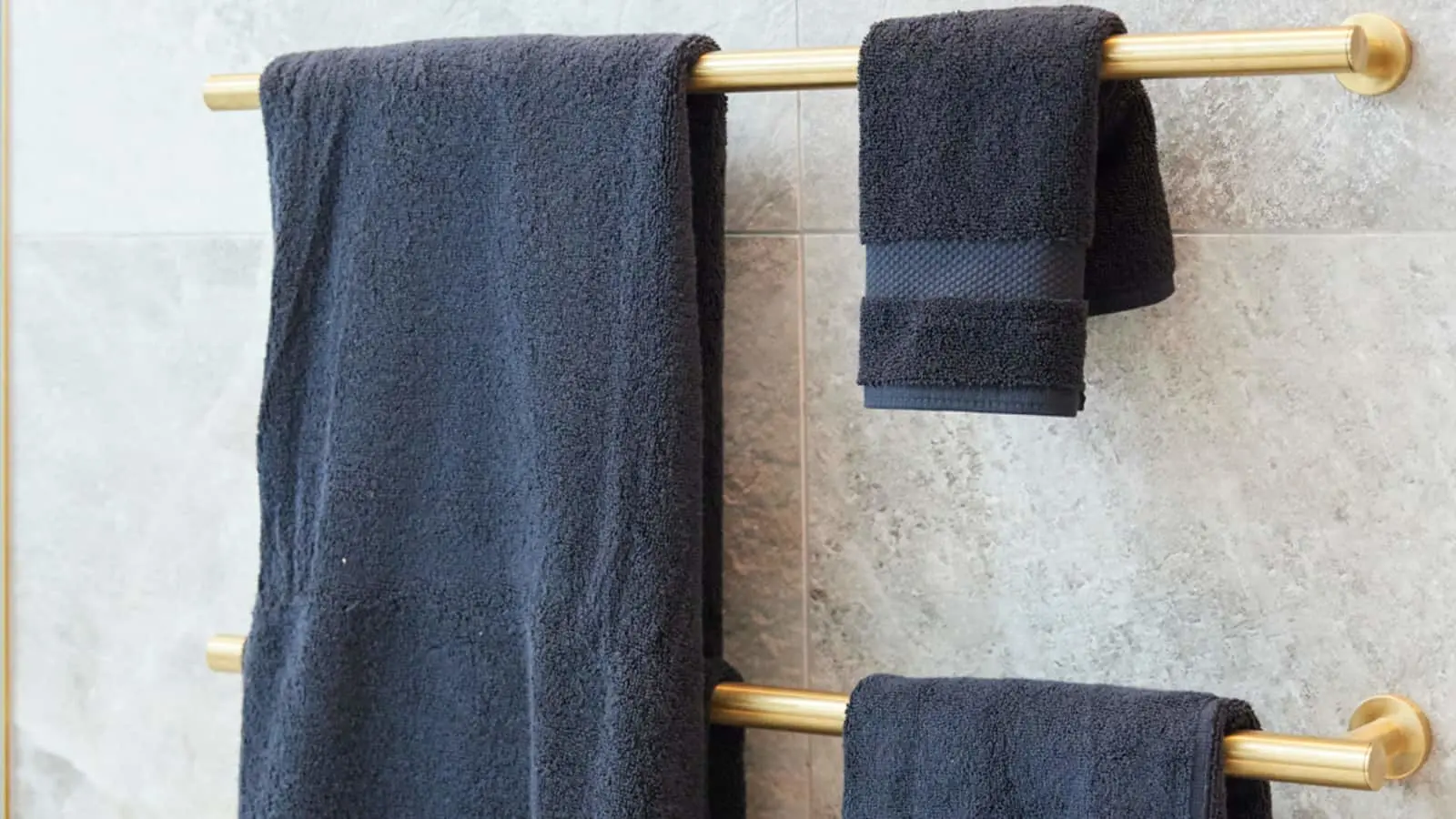 Navy blue towels hanging on gold towel bars mounted on a light gray tiled bathroom wall.