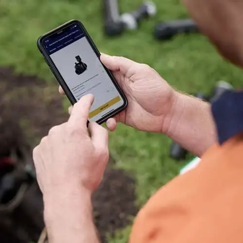 Person using smartphone app while outside on grassy lawn with tools visible in background.