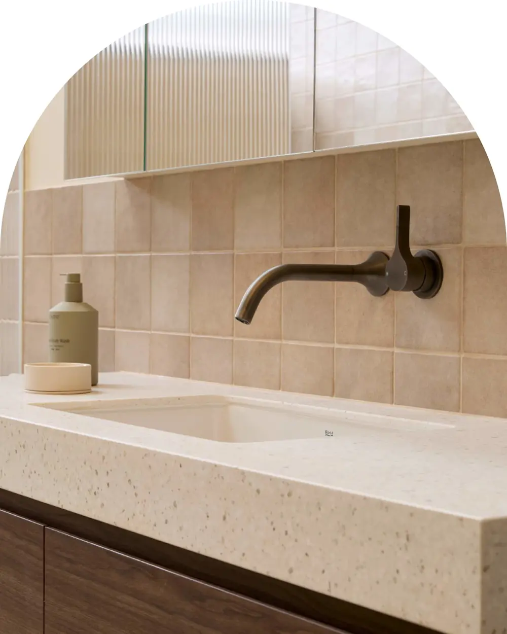 Modern bathroom sink with bronze wall-mounted faucet, beige tile backsplash, and soap dispenser on terrazzo countertop.