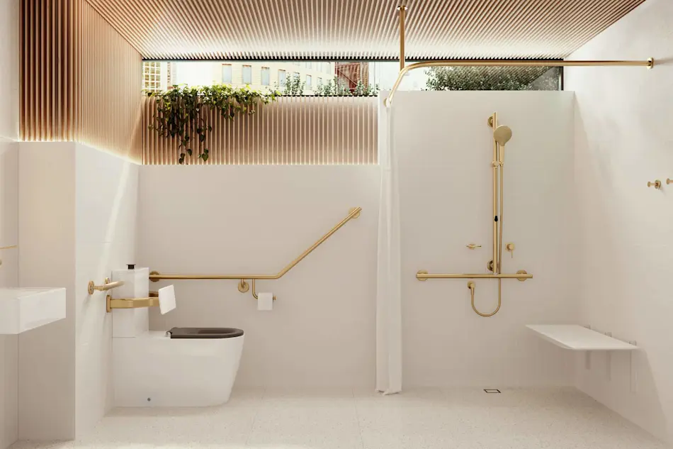 Modern accessible bathroom with white walls, gold fixtures, wooden ceiling slats, and plants near a window above.