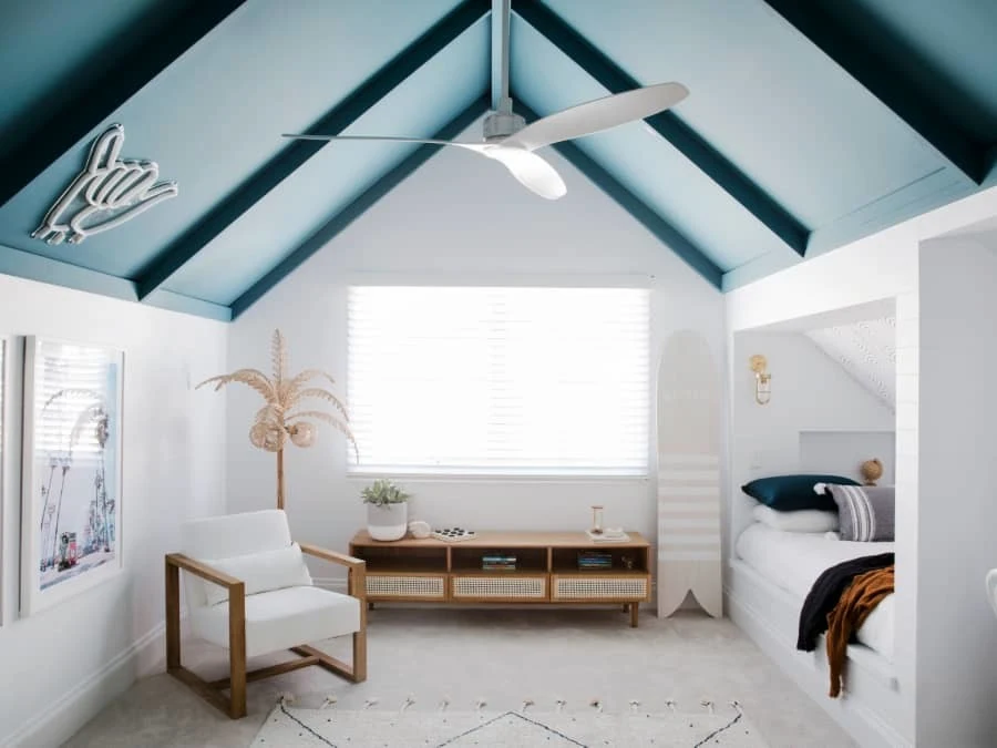 Modern bedroom with blue vaulted ceiling, white walls, wooden furniture, and a built-in bed nook with window.