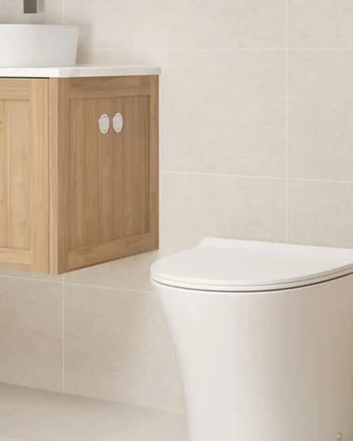 Modern bathroom with white toilet and wooden vanity cabinet with white countertop against beige tiled walls.