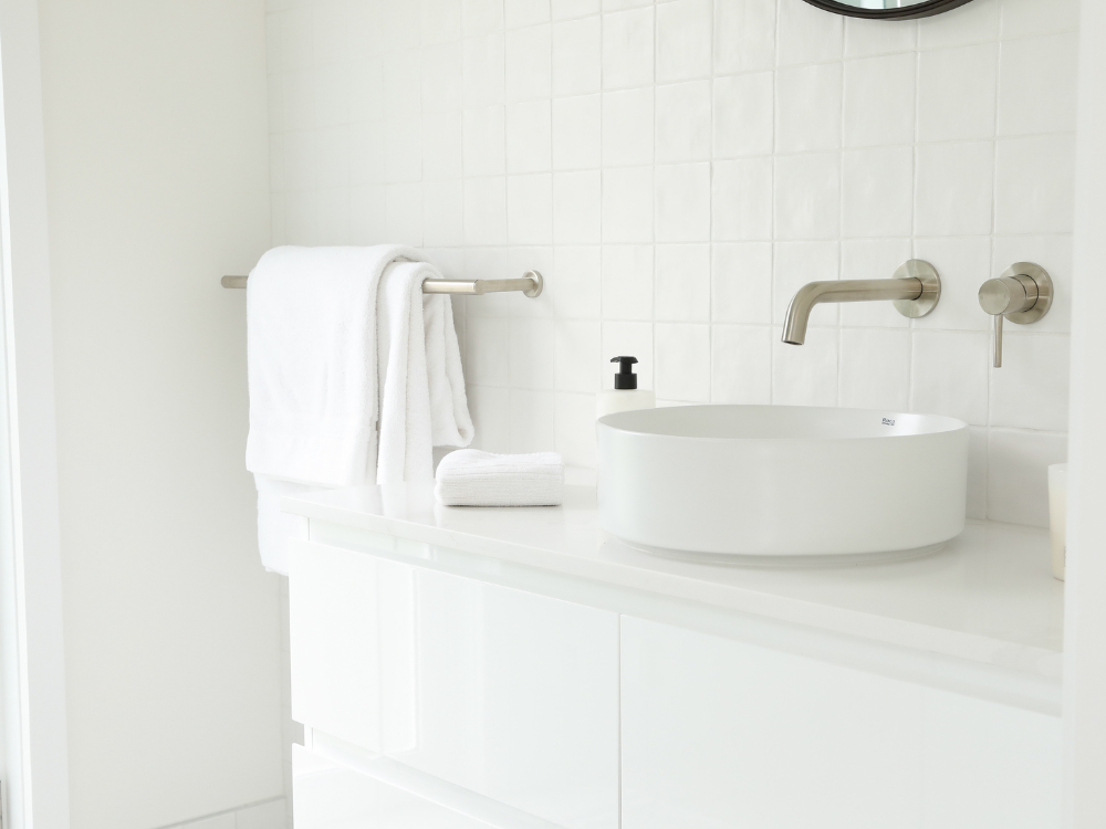 Modern white bathroom with round vessel sink, wall-mounted faucet, and neatly folded towels on a white vanity.