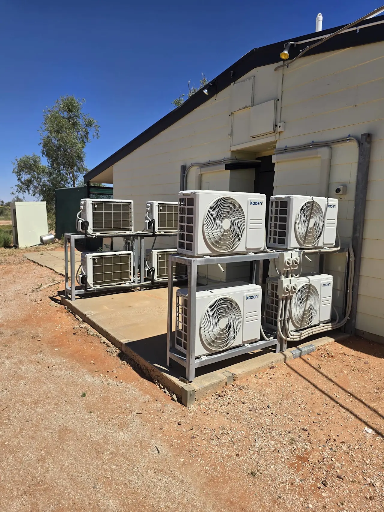 Multiple Kaden air conditioning units mounted outside a building in a dry, arid landscape under clear blue sky.