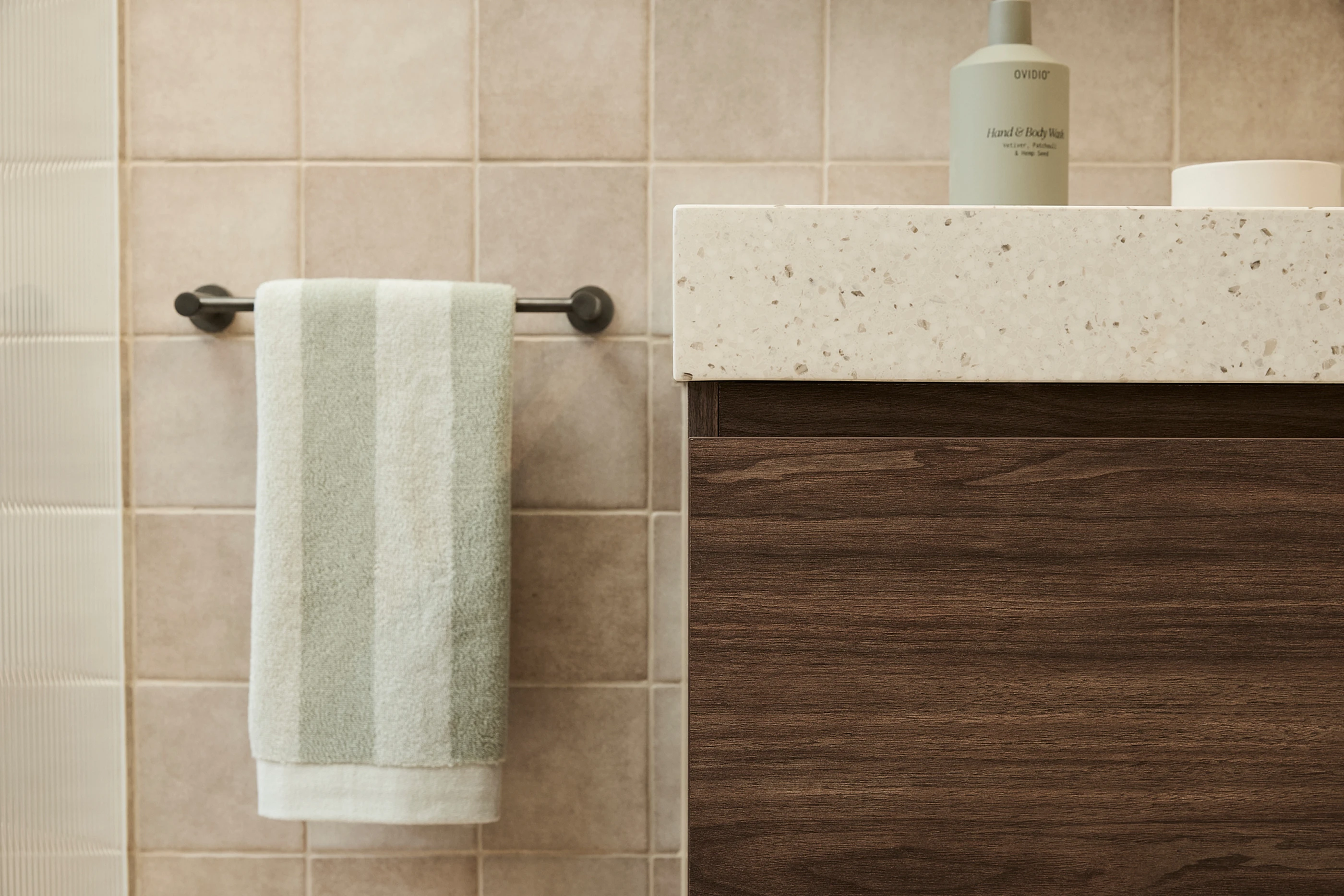 Modern bathroom with mint green towel on rack, stone countertop on wooden vanity, and hand wash bottle.