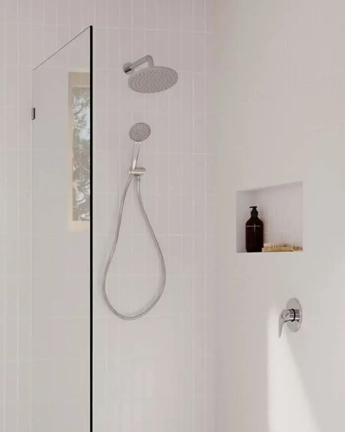 Modern white tiled shower with rainfall and handheld showerheads, glass panel, and built-in wall niche for toiletries.