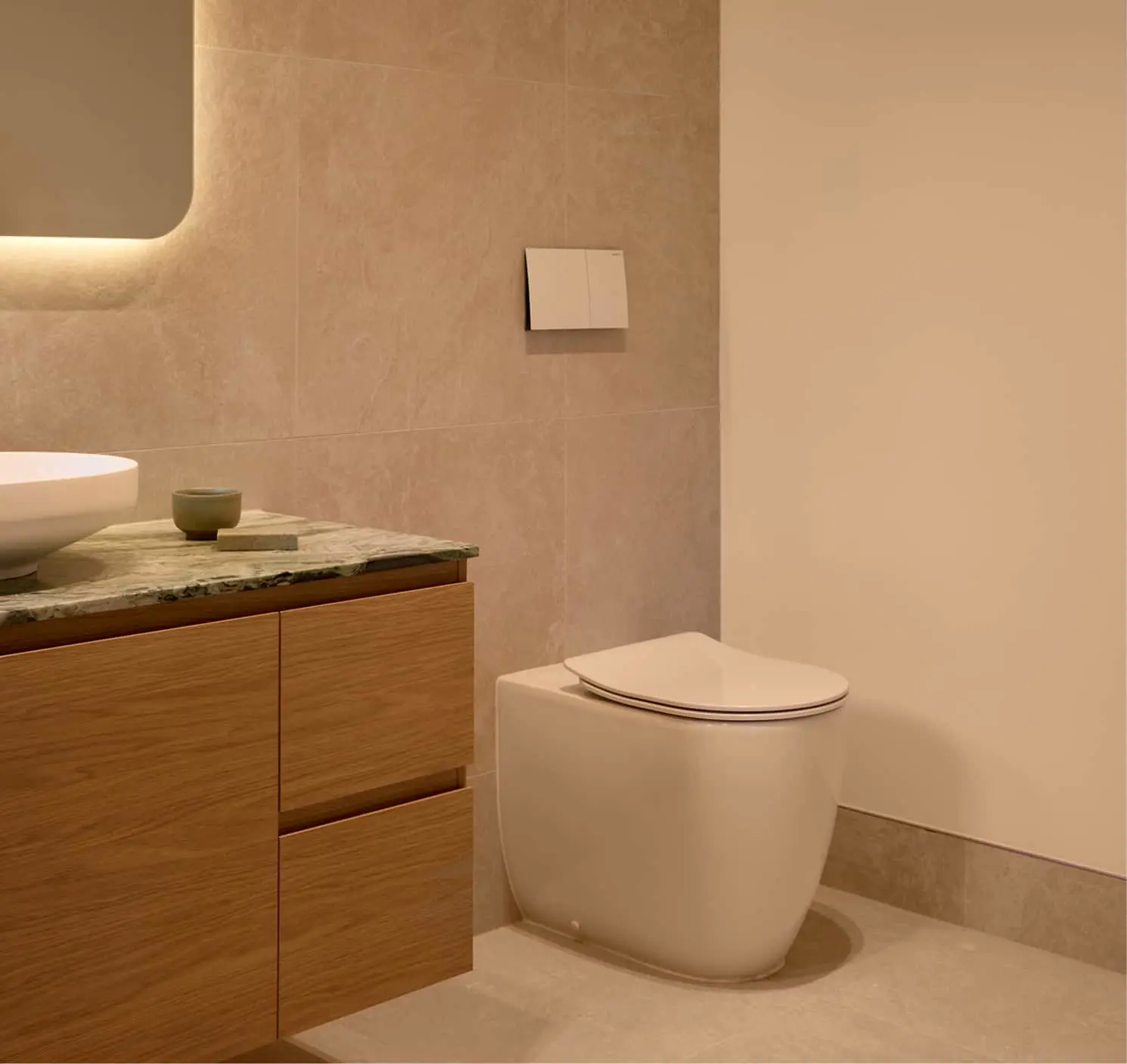Modern bathroom with beige stone walls, white toilet, wooden vanity with stone countertop, and white sink.