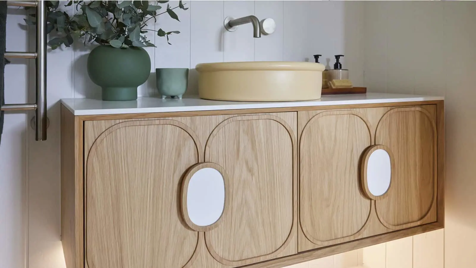 Modern bathroom vanity with wooden cabinet, cream vessel sink, green plant, and minimalist fixtures.