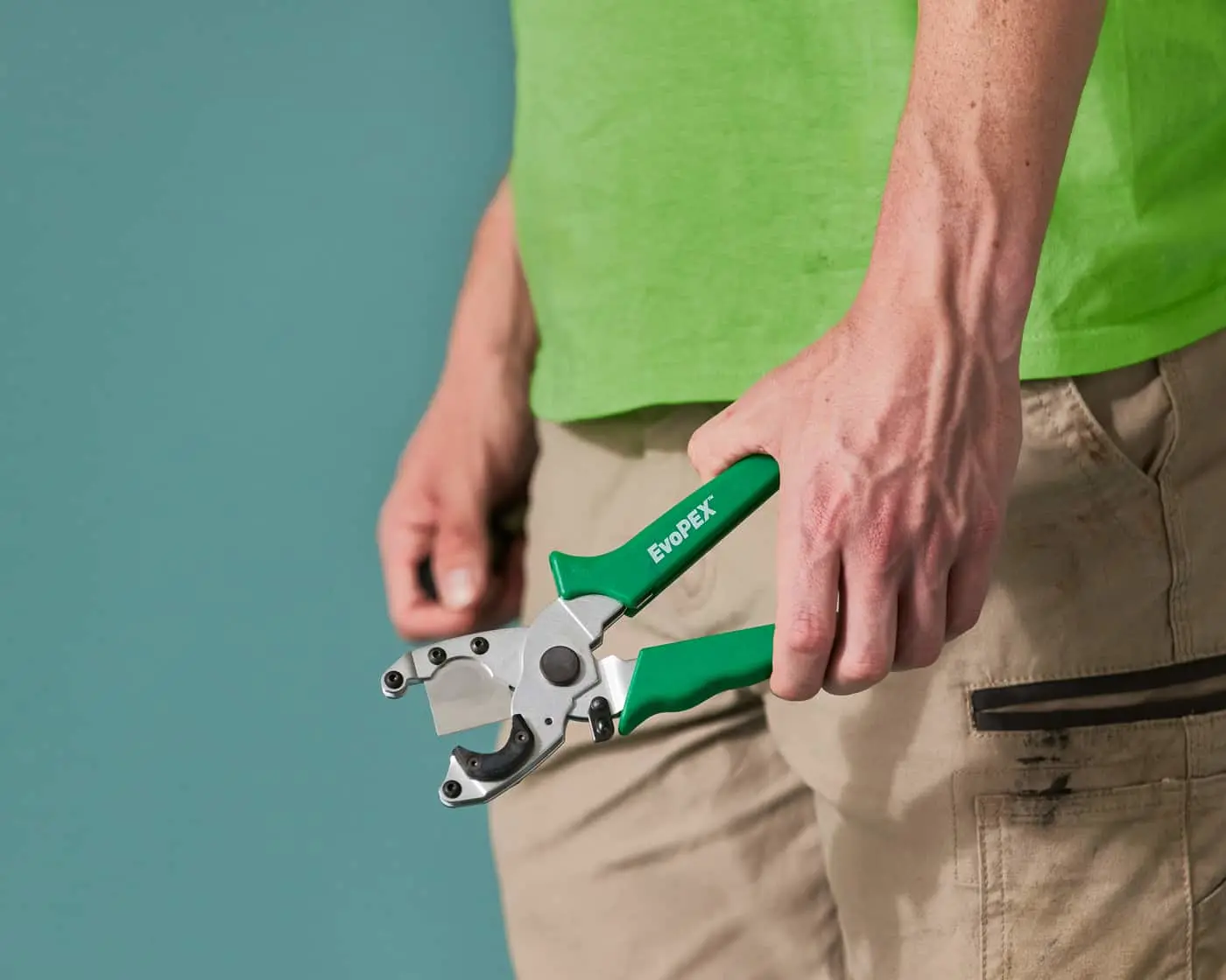 Person in bright green shirt holding green-handled EvoPEX pipe cutting tool against teal background.