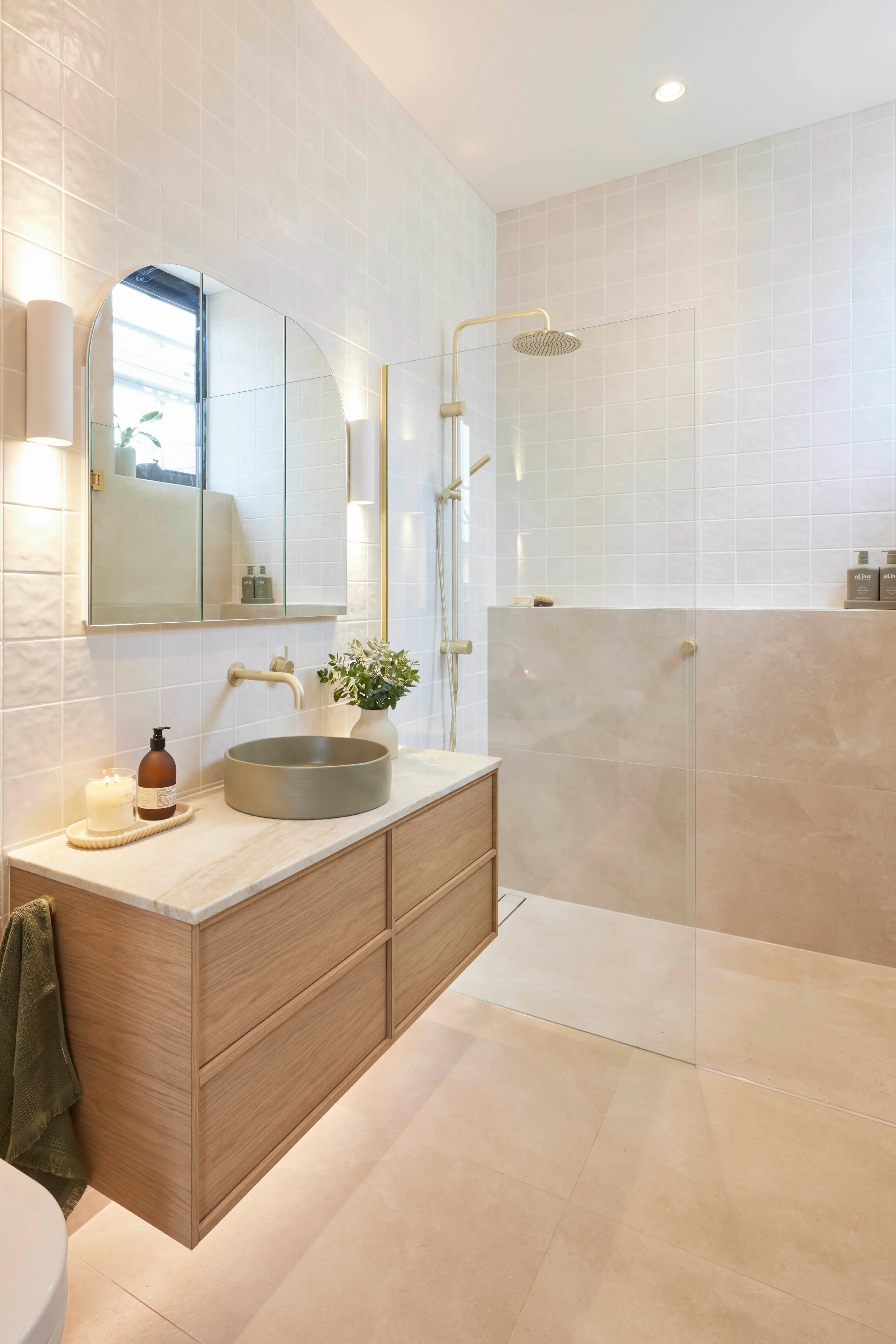 Modern bathroom with cream tiles, wooden vanity, round sink, gold fixtures, and glass shower enclosure.