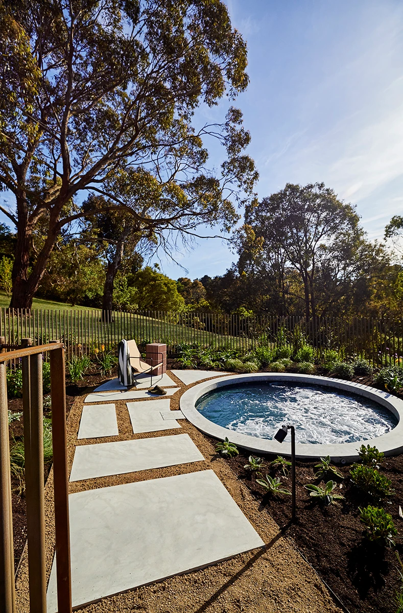 Outdoor circular hot tub with stone pavers leading to a lounge chair, surrounded by garden and tall eucalyptus trees.
