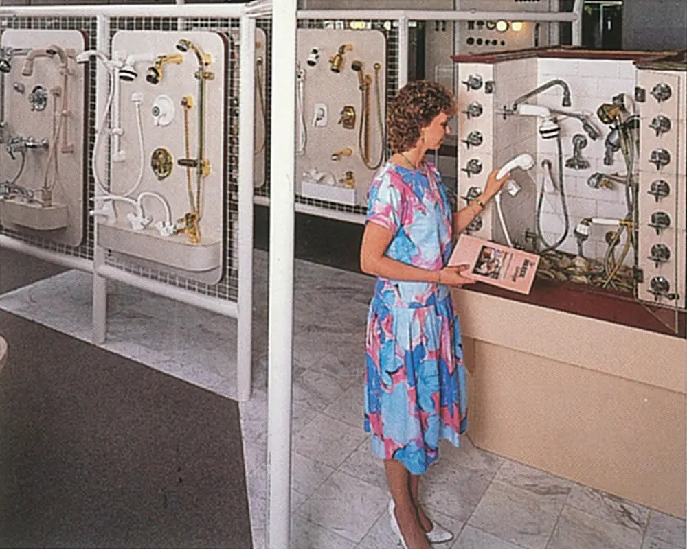 Person in blue and pink dress examining bathroom fixtures and shower heads displayed on showroom wall panels.