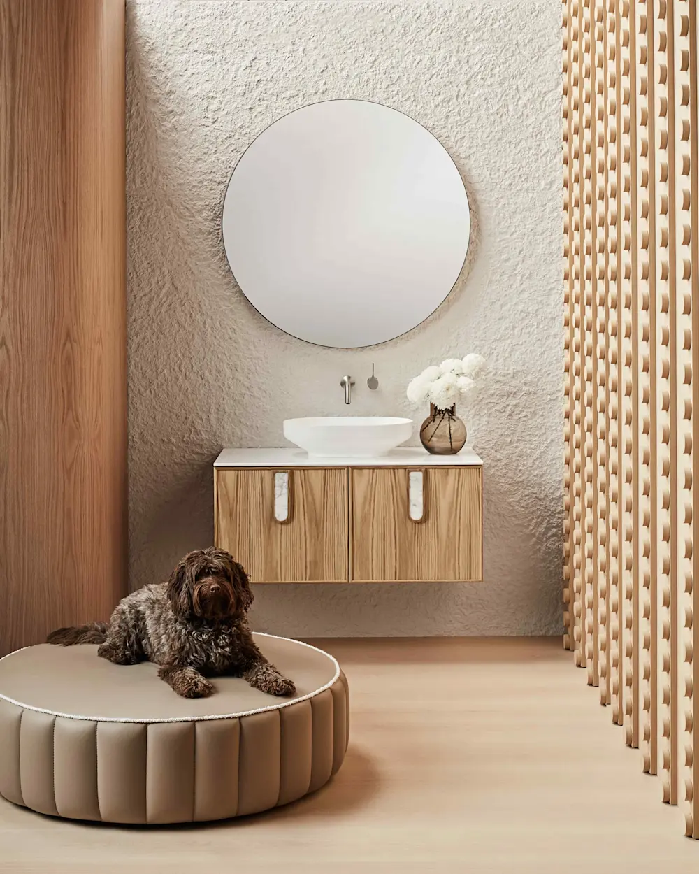 Modern bathroom with round mirror, wooden vanity, white sink, and brown dog resting on circular beige ottoman.