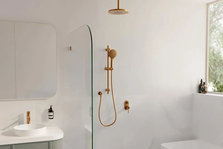 Modern white bathroom with brass fixtures featuring a rainfall showerhead, handheld sprayer, and sink beside a glass partition.