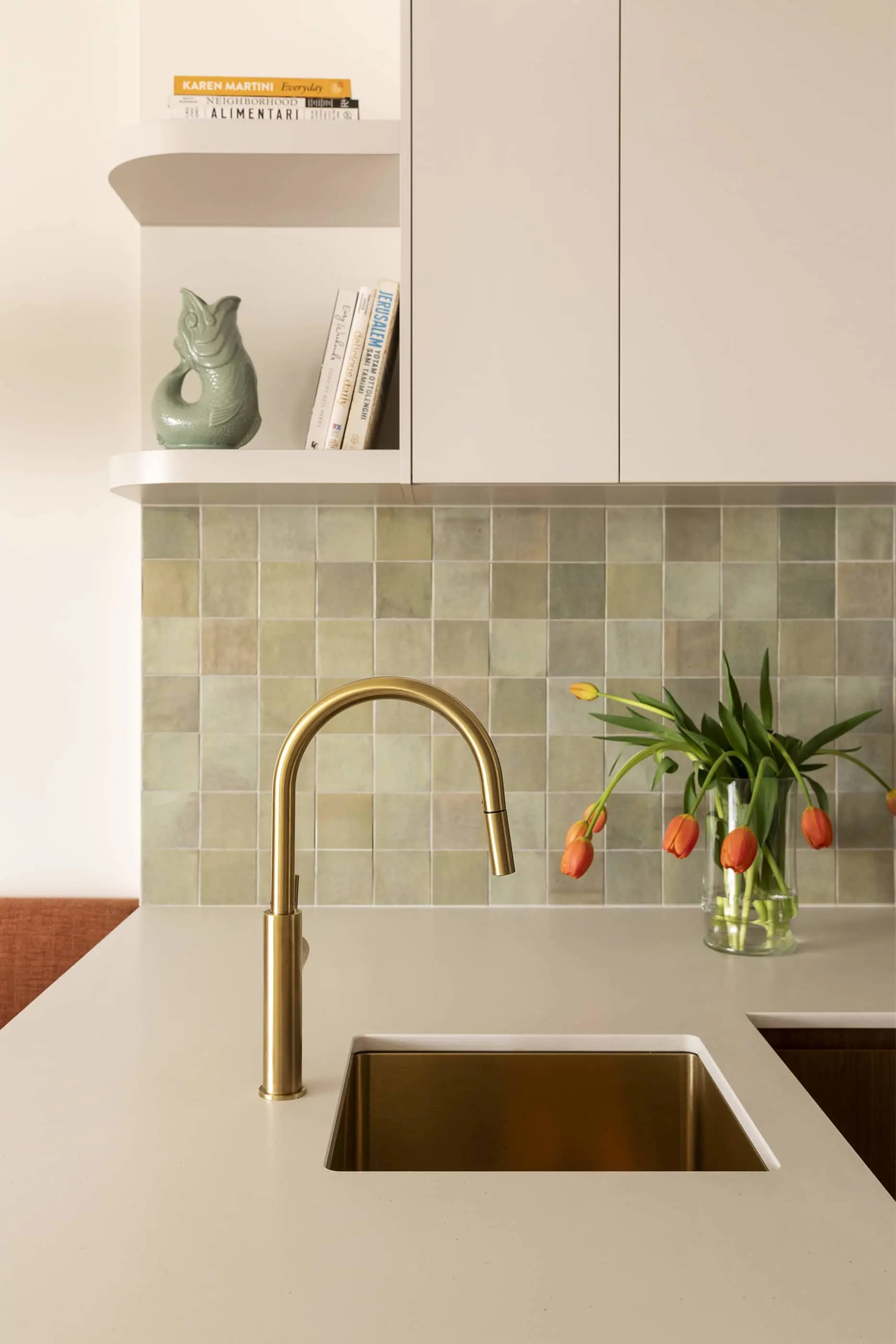 Modern kitchen with brass faucet, square sink, green tile backsplash, open shelving, and orange tulips in a vase.