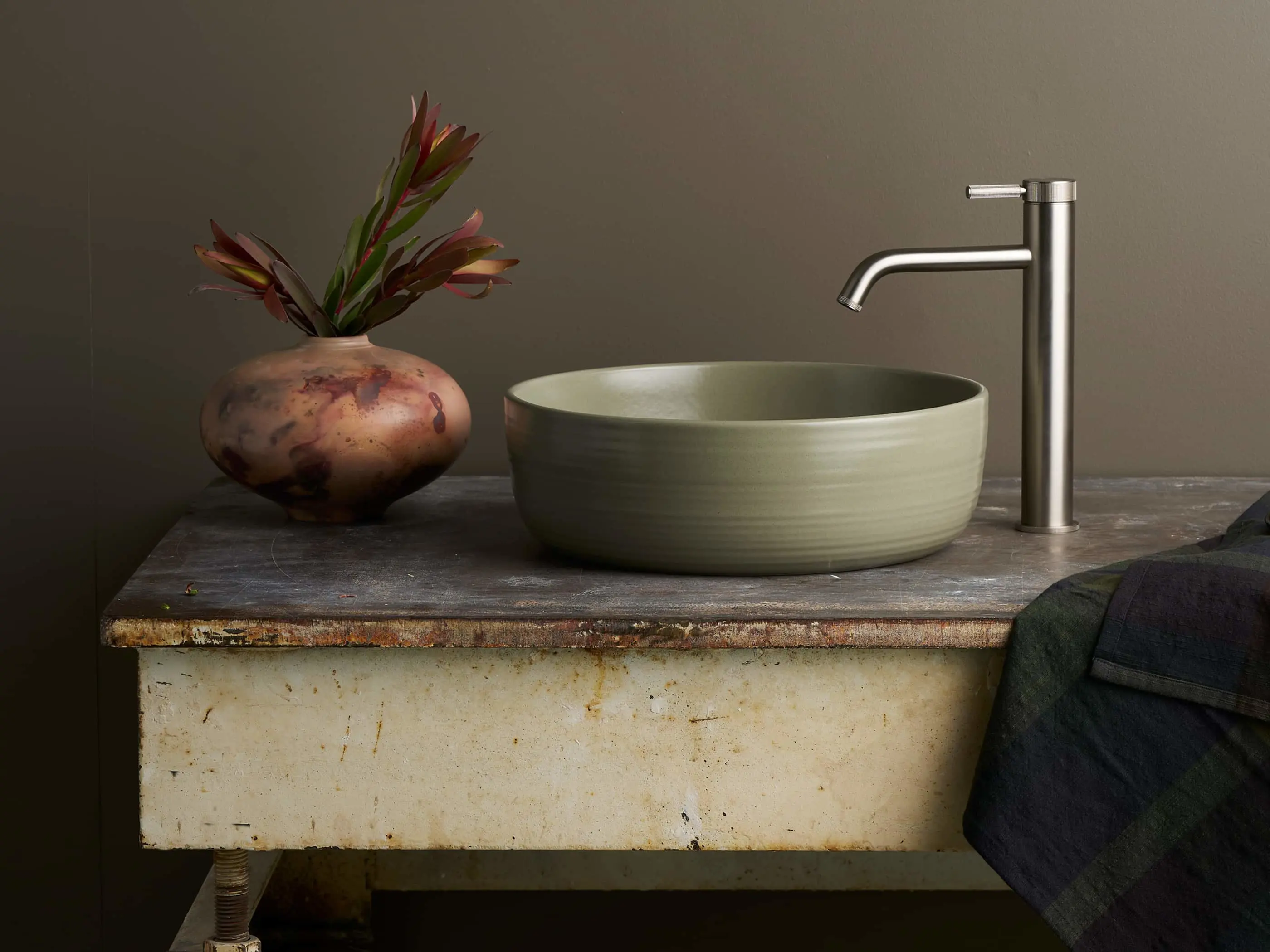 Sage green ceramic basin, stainless steel faucet, and decorative vase with red flowers.