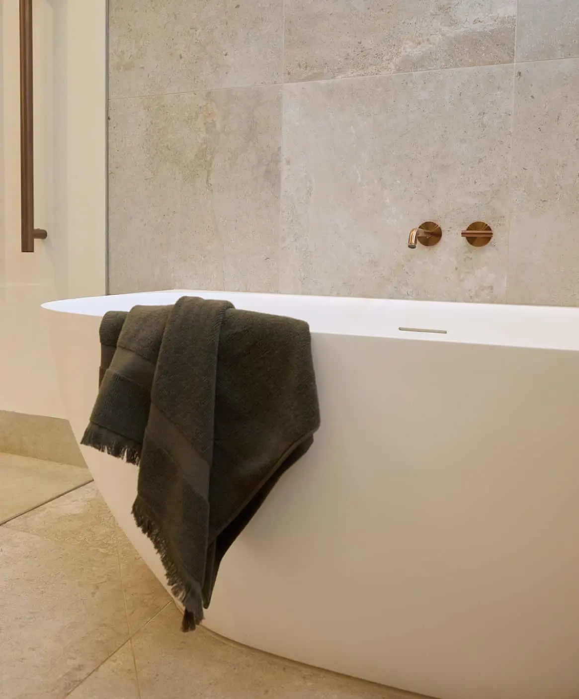 Modern bathroom with white freestanding bathtub and dark towels draped over the tub edge.