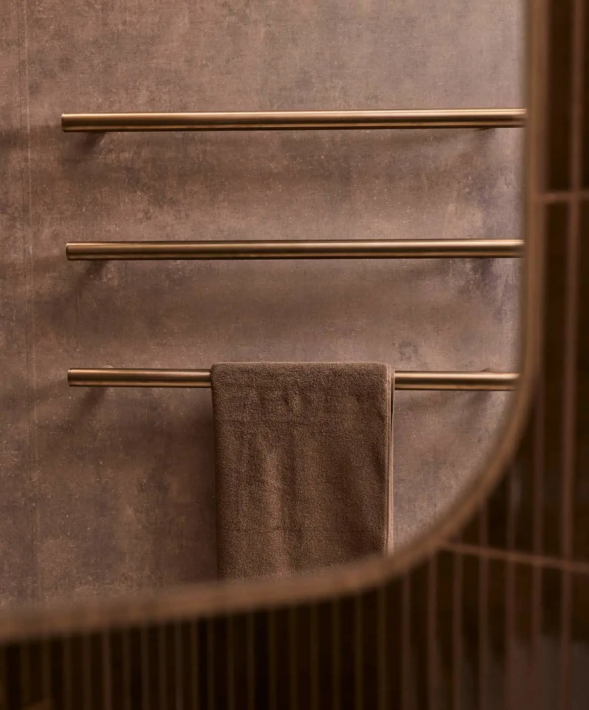 Modern bathroom with brass towel rails mounted on textured brown walls, featuring brown towels and vertical paneling.