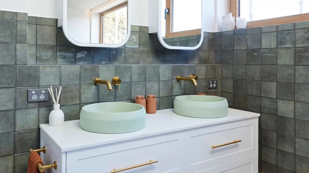 Modern bathroom with mint green vessel sinks, brass fixtures, white vanity, and green tile backsplash.