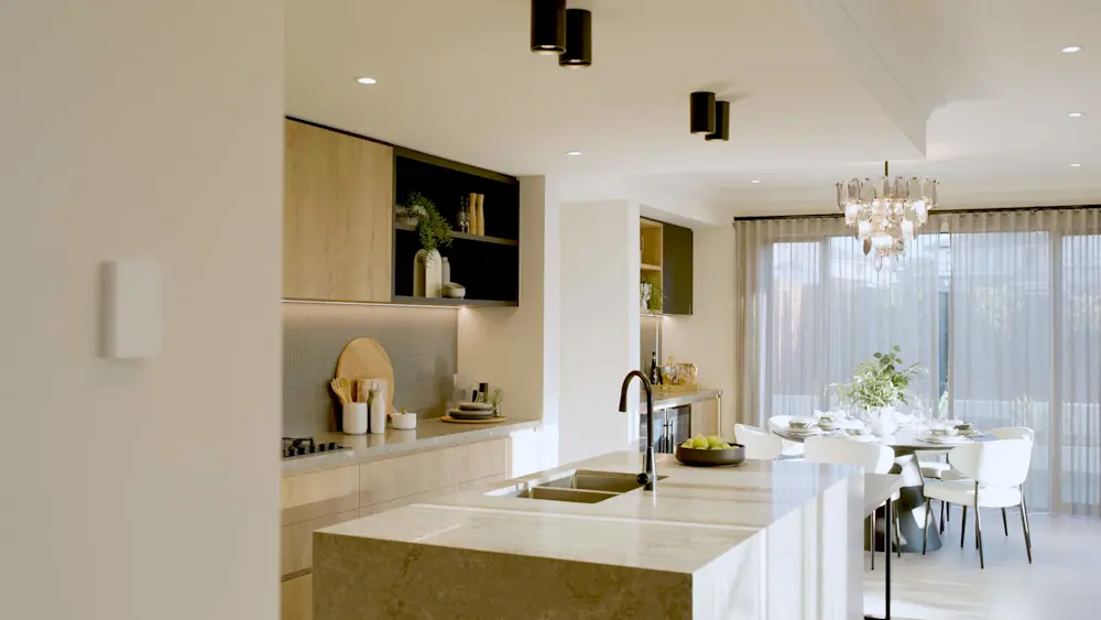 Modern kitchen with marble island, light wood cabinets, and dining area with crystal chandelier and sheer curtains.