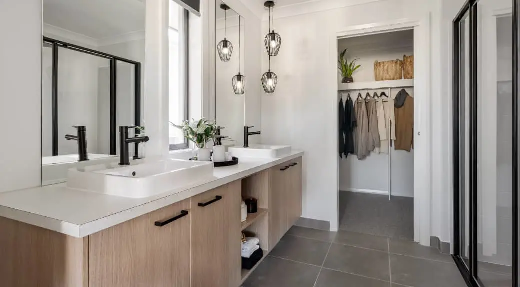 Modern bathroom with double sink vanity, pendant lights, and walk-in closet visible through doorway with hanging clothes.