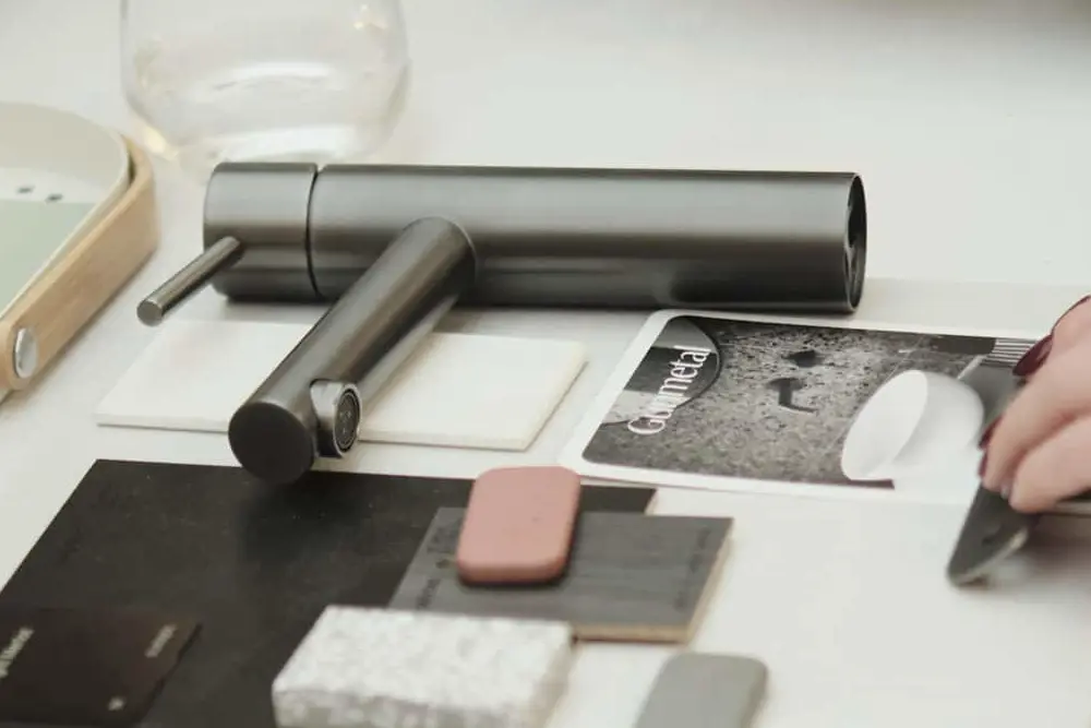 Hands arranging material samples on a white table with design tools, notebooks, and a small plant in the background.