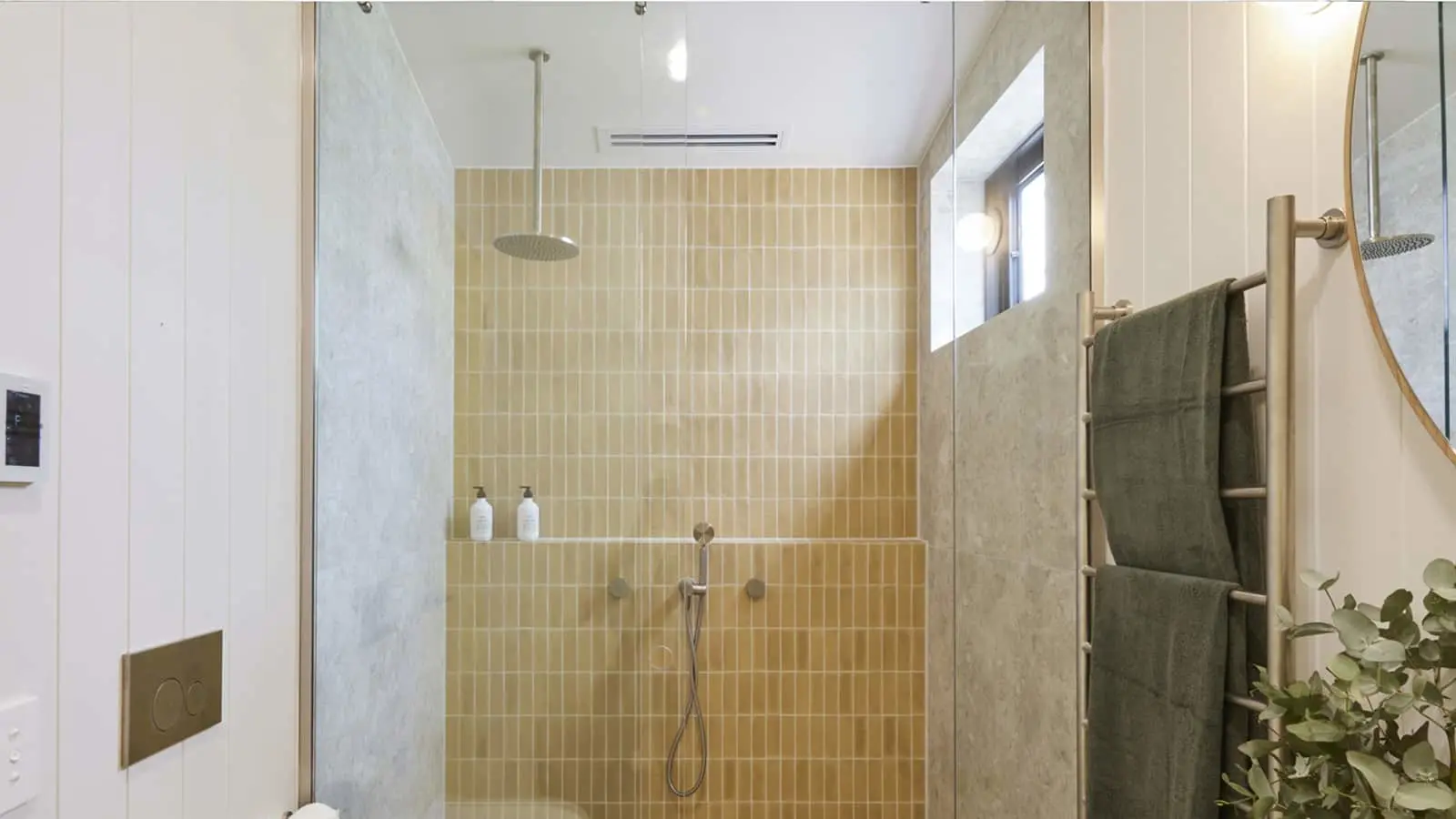 Modern bathroom with beige tiled shower, rainfall showerhead, green towels on rack, and small window.