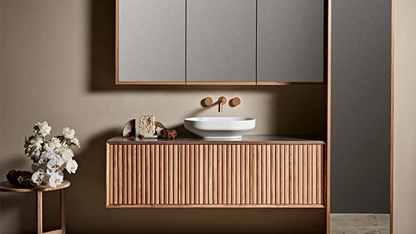Modern bathroom with wooden vanity, white vessel sink, wall-mounted brass faucet, mirror cabinet, and white flowers.