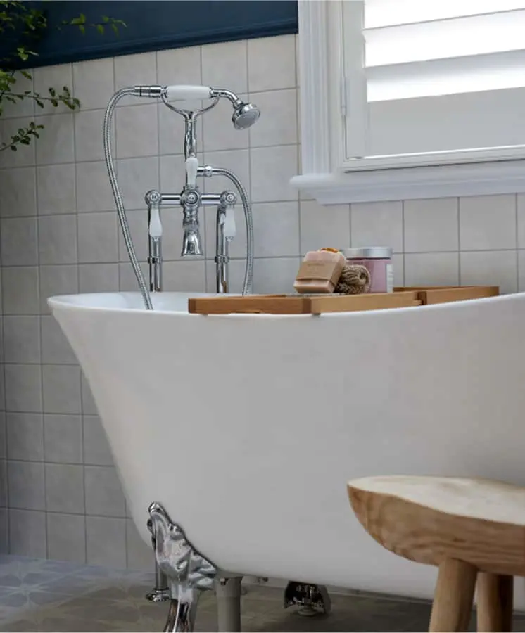 White clawfoot bathtub with chrome fixtures, wooden bath caddy holding soap and containers, next to a small wooden stool.