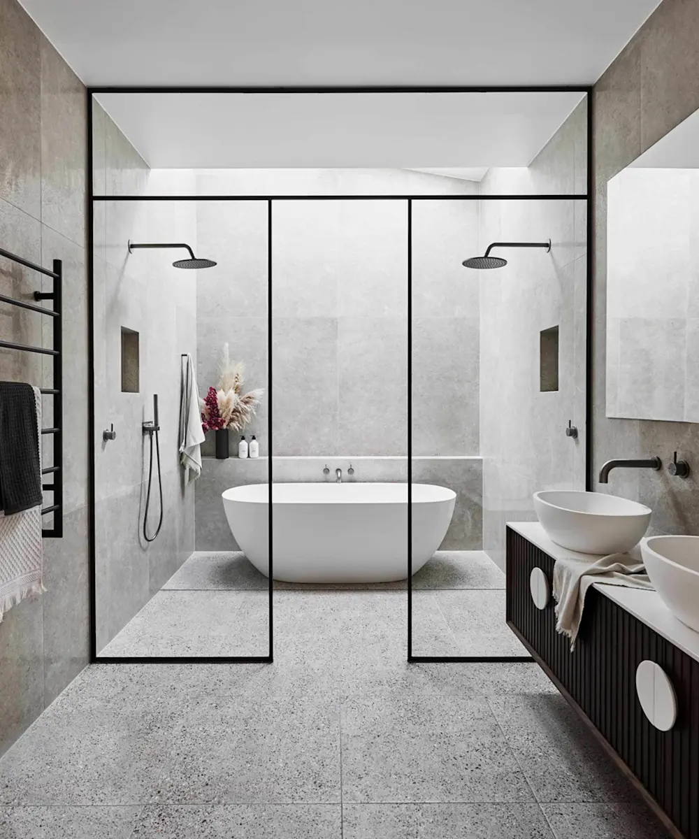 Modern bathroom with glass-enclosed shower area, freestanding white bathtub, gray stone tiles, and vessel sinks on dark vanity.