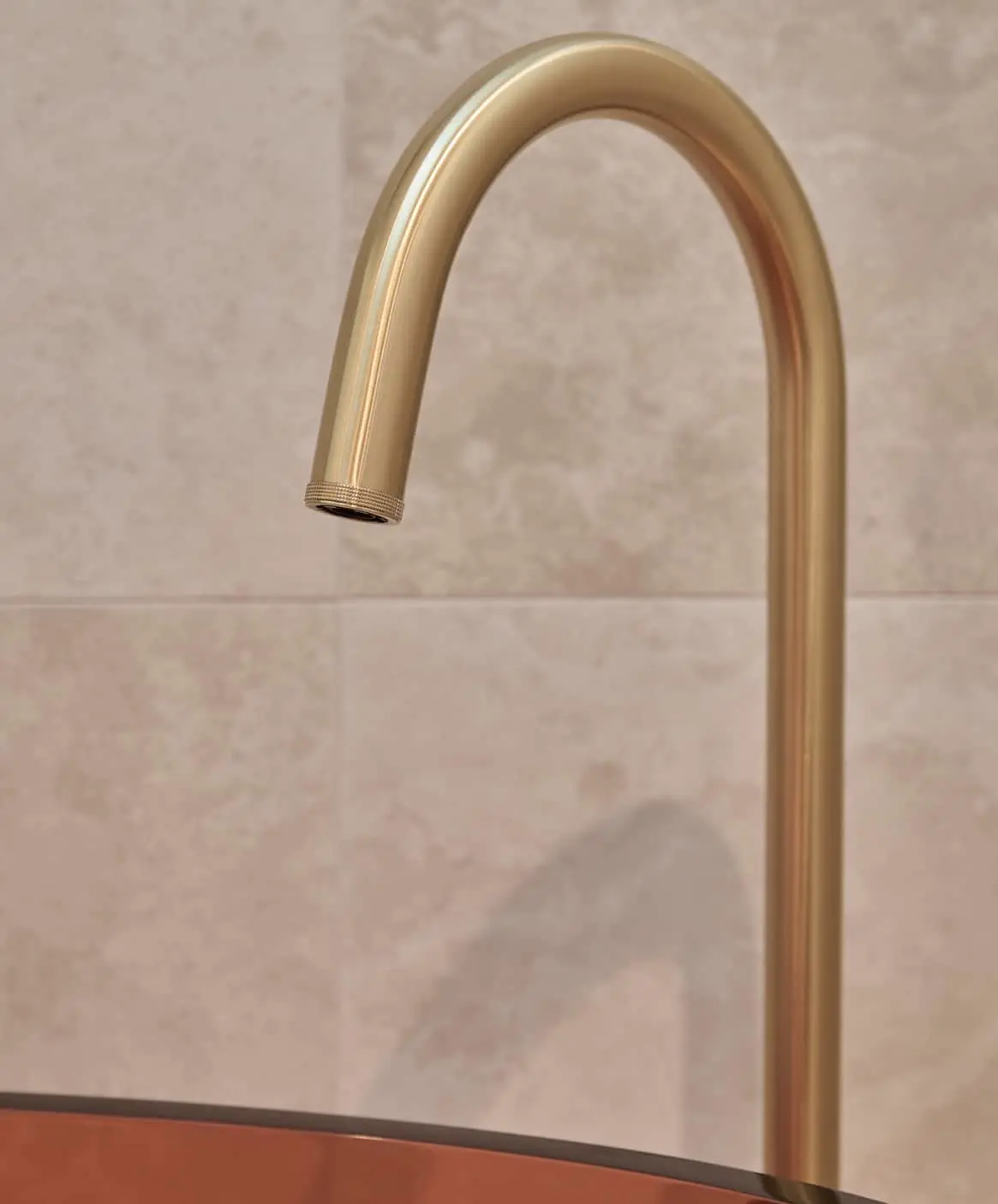 Gold bathroom floor mounted outlet with minimalist design against pink tile walls.