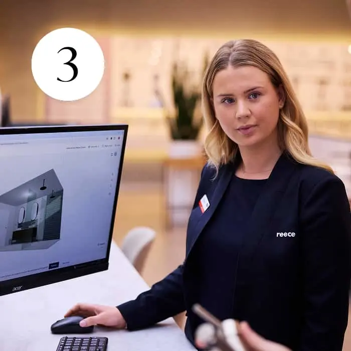 A Reece staff member sits at a desk with a computer showing a 3D bathroom design. Number 3 is displayed in the top corner.
