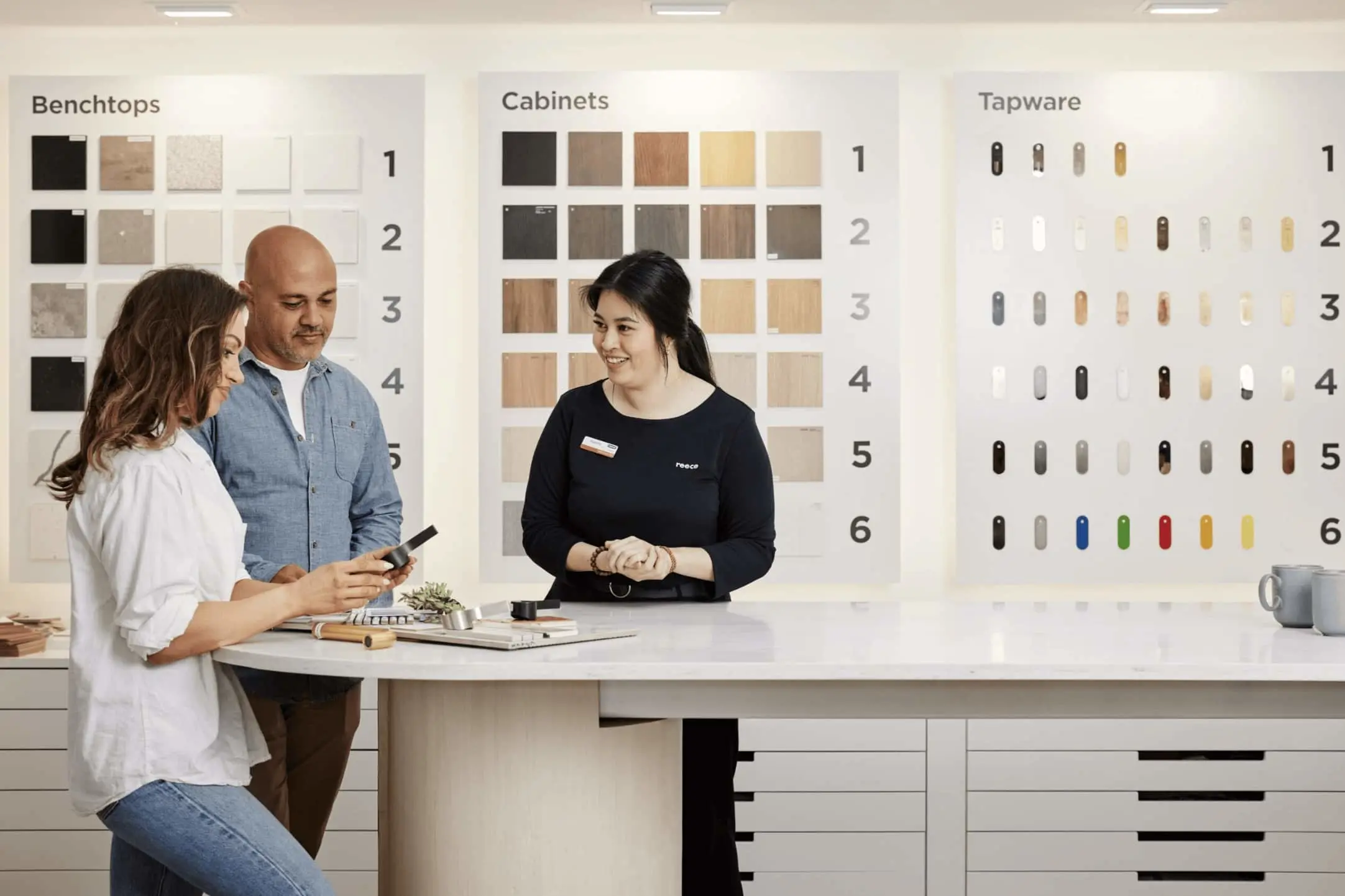 Couple consulting with bathroom consultant in showroom with sample displays of benchtops, cabinets, and tapware options.